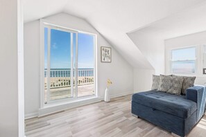 A room with a balcony, a sofa, a vase with flowers, and a framed picture on the wall.