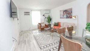 Ein modernes Wohnzimmer mit einer Sofagarnitur, einem Couchtisch und einem Essbereich mit Stühlen und einem Glastisch.