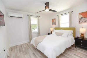A bedroom with a bed, bedside lamps, a ceiling fan, and an air conditioning unit.