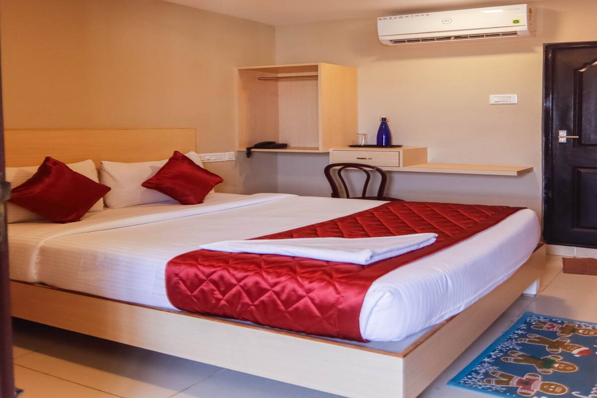 Habitación de hotel con cama, escritorio, silla, ventilador de techo y aire acondicionado, además de una puerta.