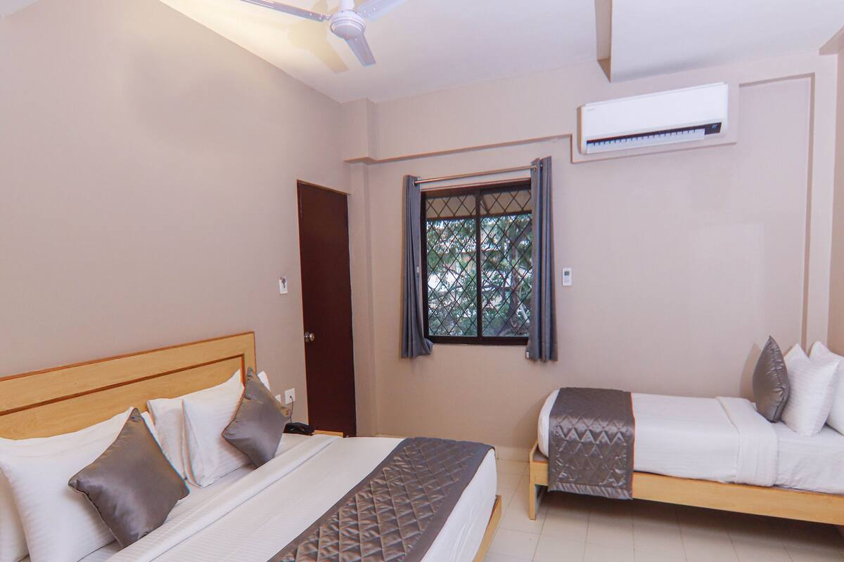 Una habitación de hotel con una cama grande, una cama más pequeña, un ventanal con vistas, un equipo de aire acondicionado y un ventilador de techo.
