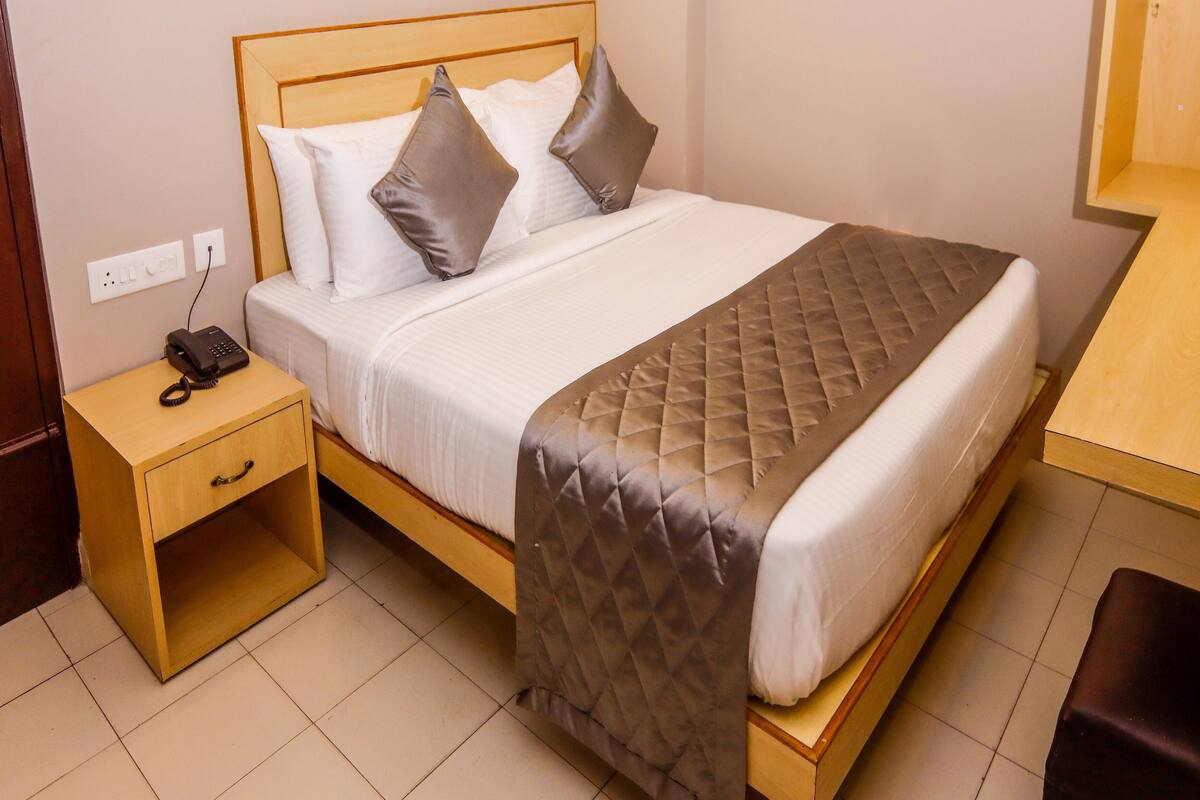 Una cama bien hecha con un edredón acolchado, un teléfono en la mesita de noche y un tocador de madera con un cajón.