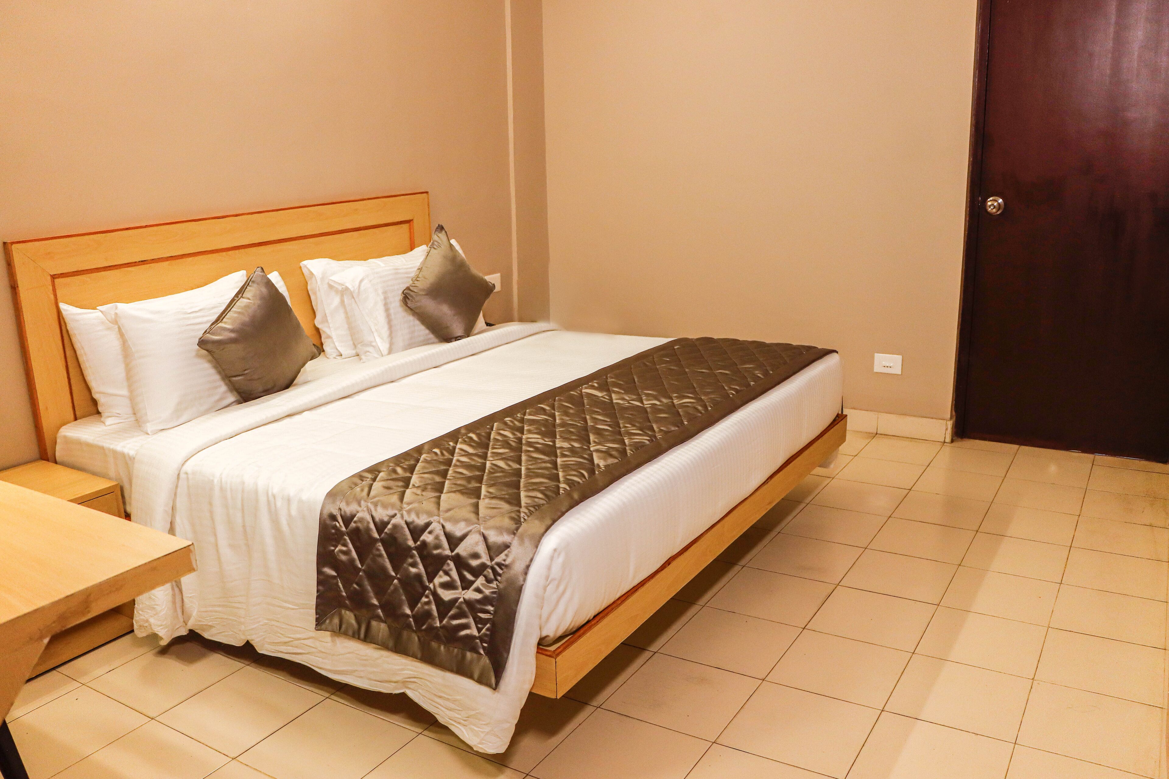 Een net opgemaakt bed met een houten hoofdbord, witte beddengoed en een bruine geborduurde plaid.