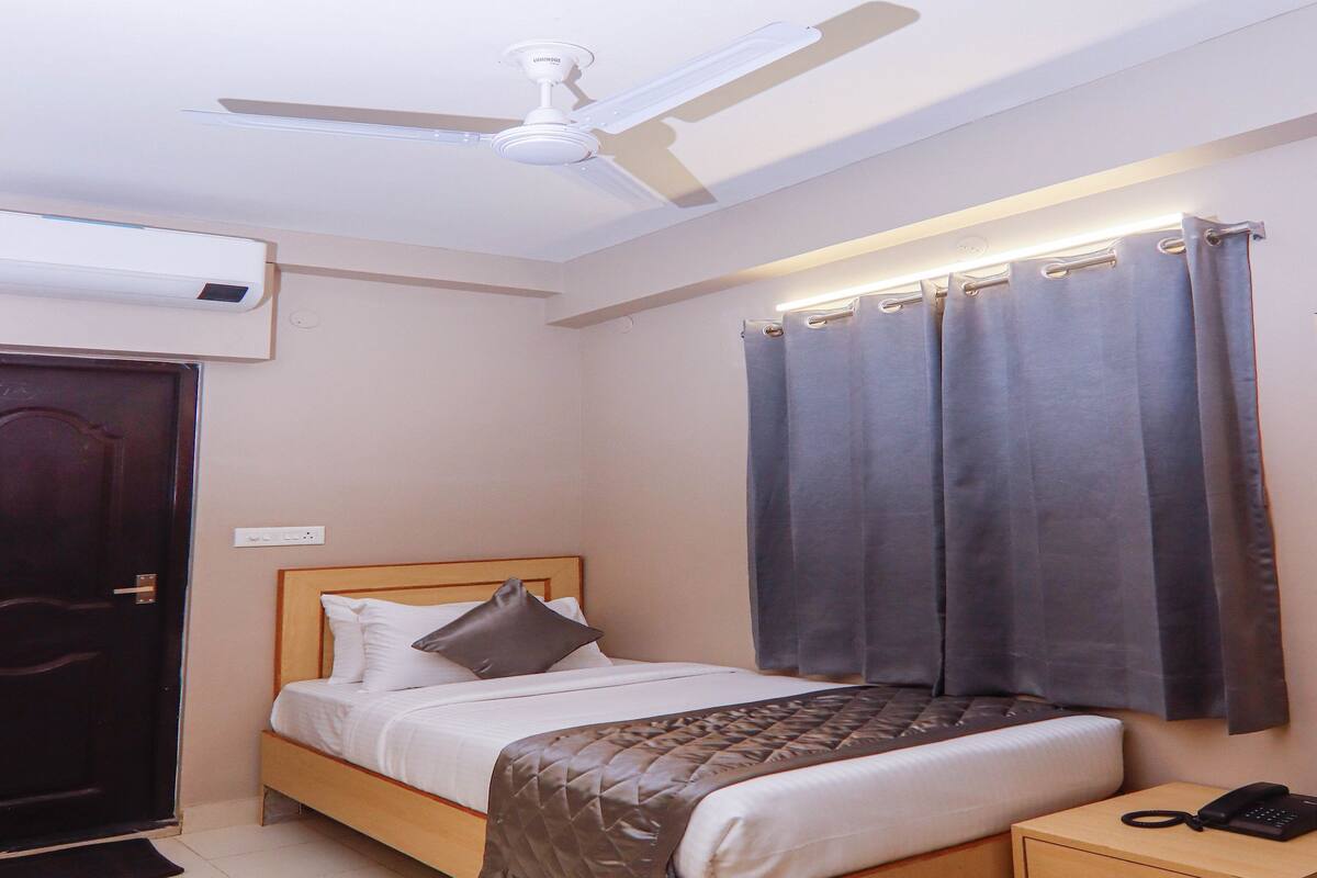 Un dormitorio con cama, mesita de noche con teléfono, ventilador de techo y ventana con cortinas.