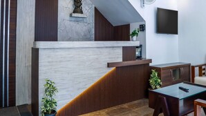 Ein moderner Empfangsbereich mit Marmorwand, Holzvertäfelung, einer Statue, einem Deckenventilator, einem Fernseher und einer Rezeption.