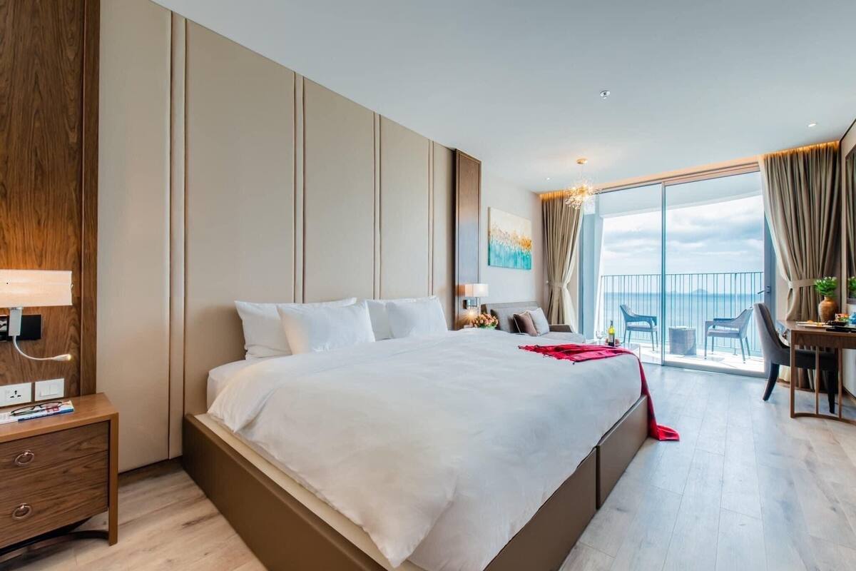 A hotel room with a large bed, a desk, and a balcony with a view.
