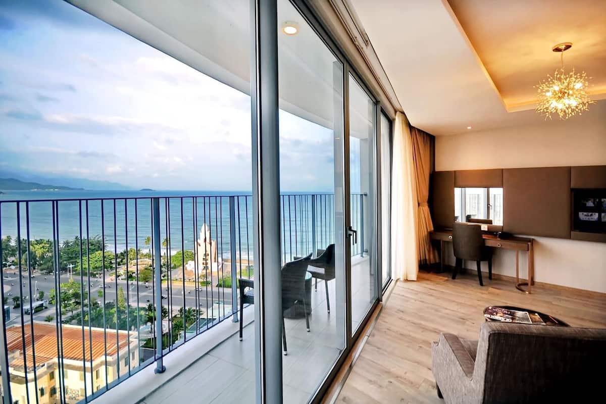 A modern living room with a large balcony overlooking a cityscape and the sea.