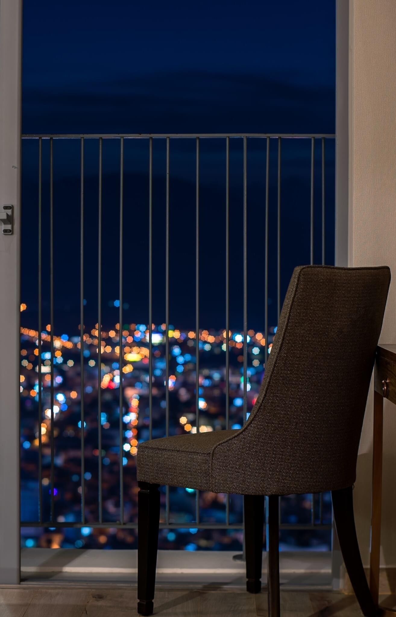 A chair by a window with a view of a cityscape at night.