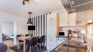 Une cuisine moderne dotée d’un four à micro-ondes encastré, d’un évier en acier inoxydable et de chaises noires disposées autour d’une table à manger en bois.