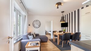 Un salon moderne comprenant un canapé, une table basse, un coin repas avec des chaises, un téléviseur et un coin cuisine avec un comptoir.