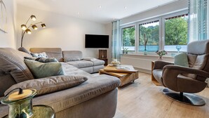 Un salon moderne comprenant un canapé, un fauteuil, une table basse et un téléviseur à écran plat.