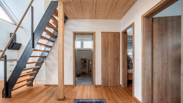 A modern interior with a wooden staircase, a hallway leading to a room, and a door.
