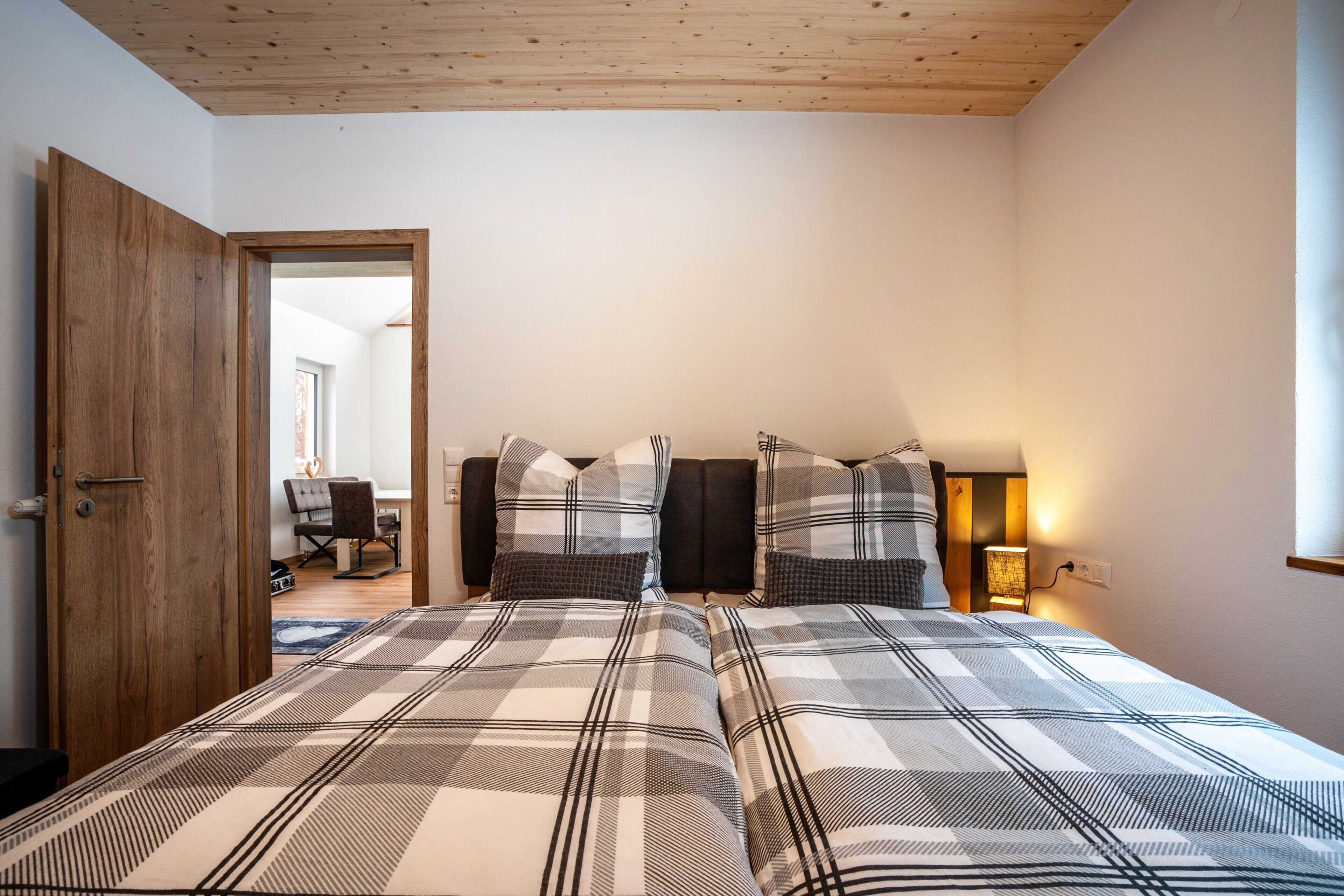 A bedroom with a large bed, a wooden door, and a desk with a chair.