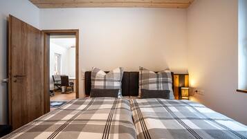 A bedroom with a large bed, a wooden door, and a desk with a chair.