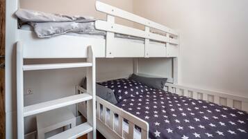 Uma cama beliche com colcha estampada em formato de estrela, cabeceira branca e uma estante.