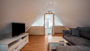 A modern loft bedroom with a sloped ceiling, a television on a wooden stand, a sofa, and a small table.