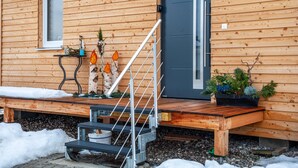 A wooden cabin with a wooden staircase, a door, and a small table with decorative items.