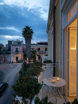 A balcony with a table and chairs, a palm tree, and a view of the street and buildings. - Casa Makrame in Syracuse (Syracuse)