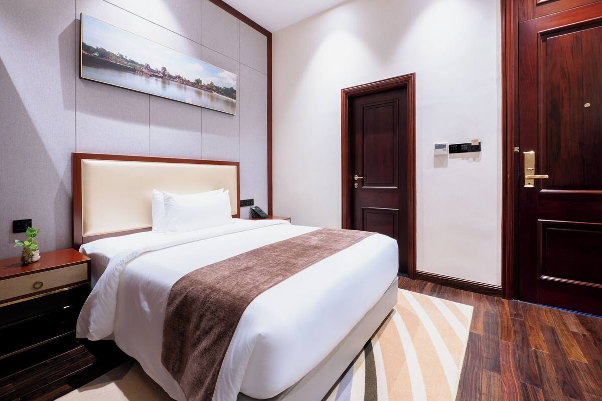 Een hotelkamer met een bed, nachtkastje en een deur.