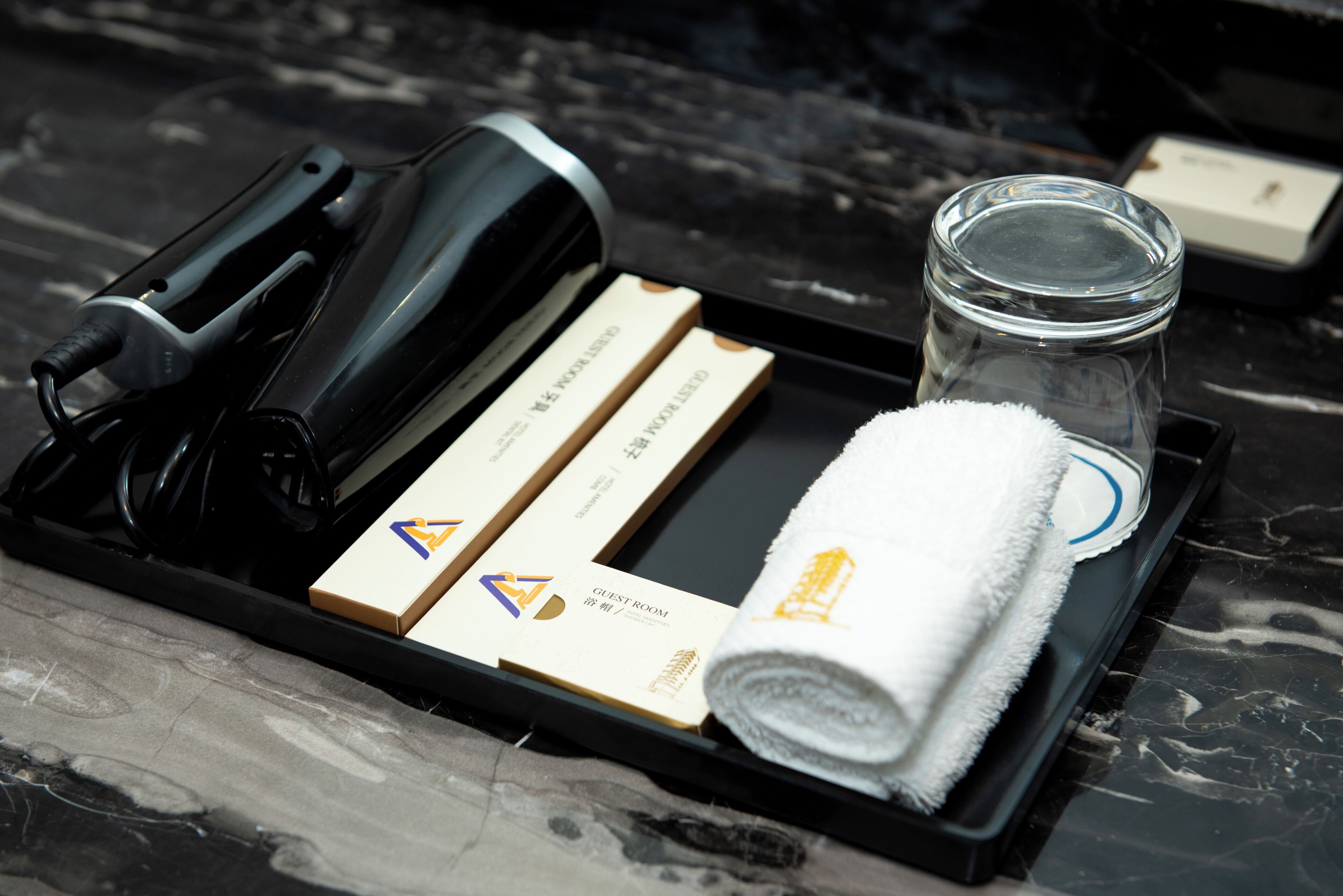 A tray with a hairdryer, a rolled towel, a glass jar, and two hotel room key cards.