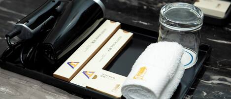 A tray with a hairdryer, a rolled towel, a glass jar, and two hotel room key cards.