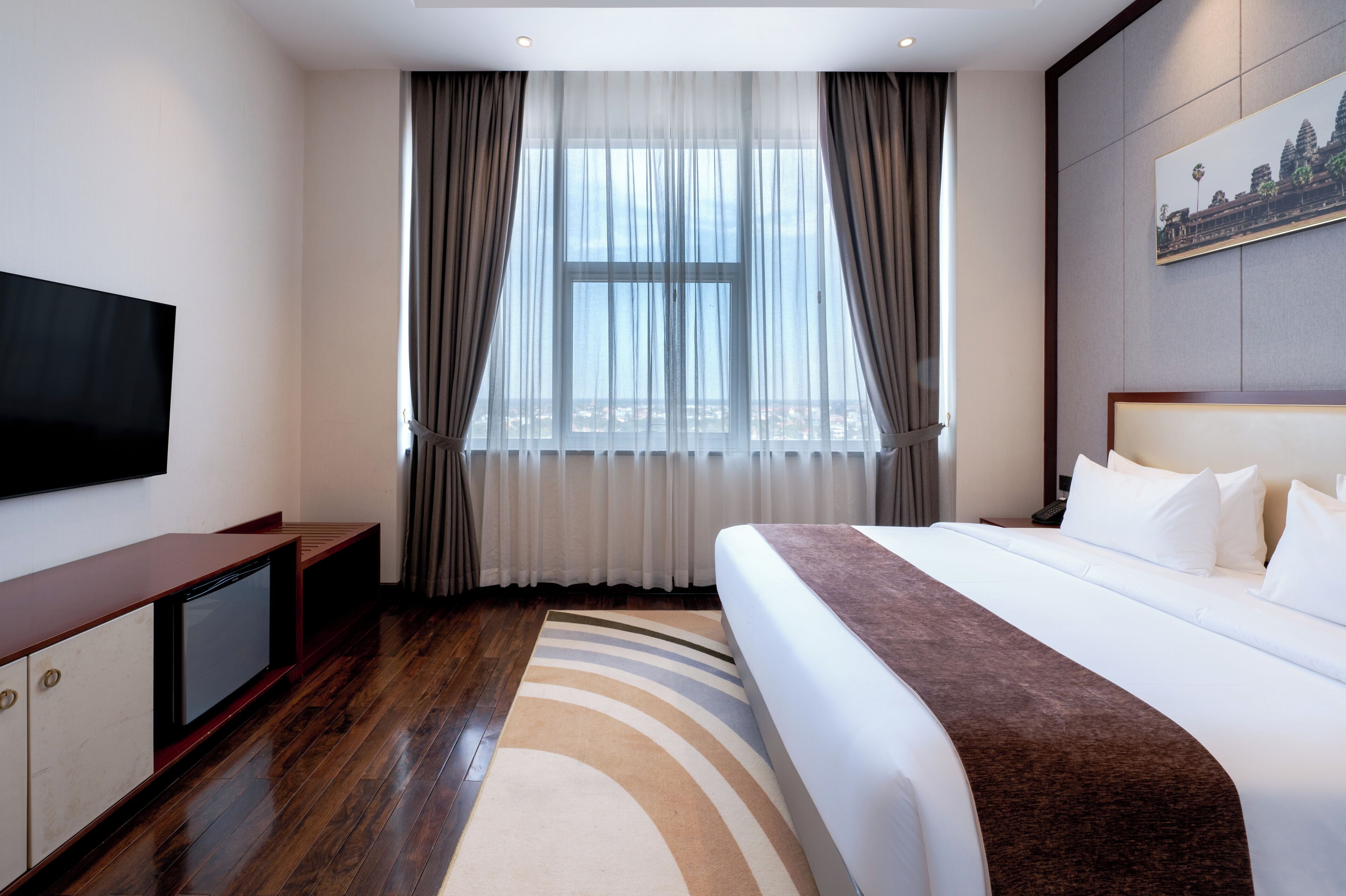 Een hotelkamer met een groot bed, een flatscreen televisie, een bureau en een raam met gordijnen.