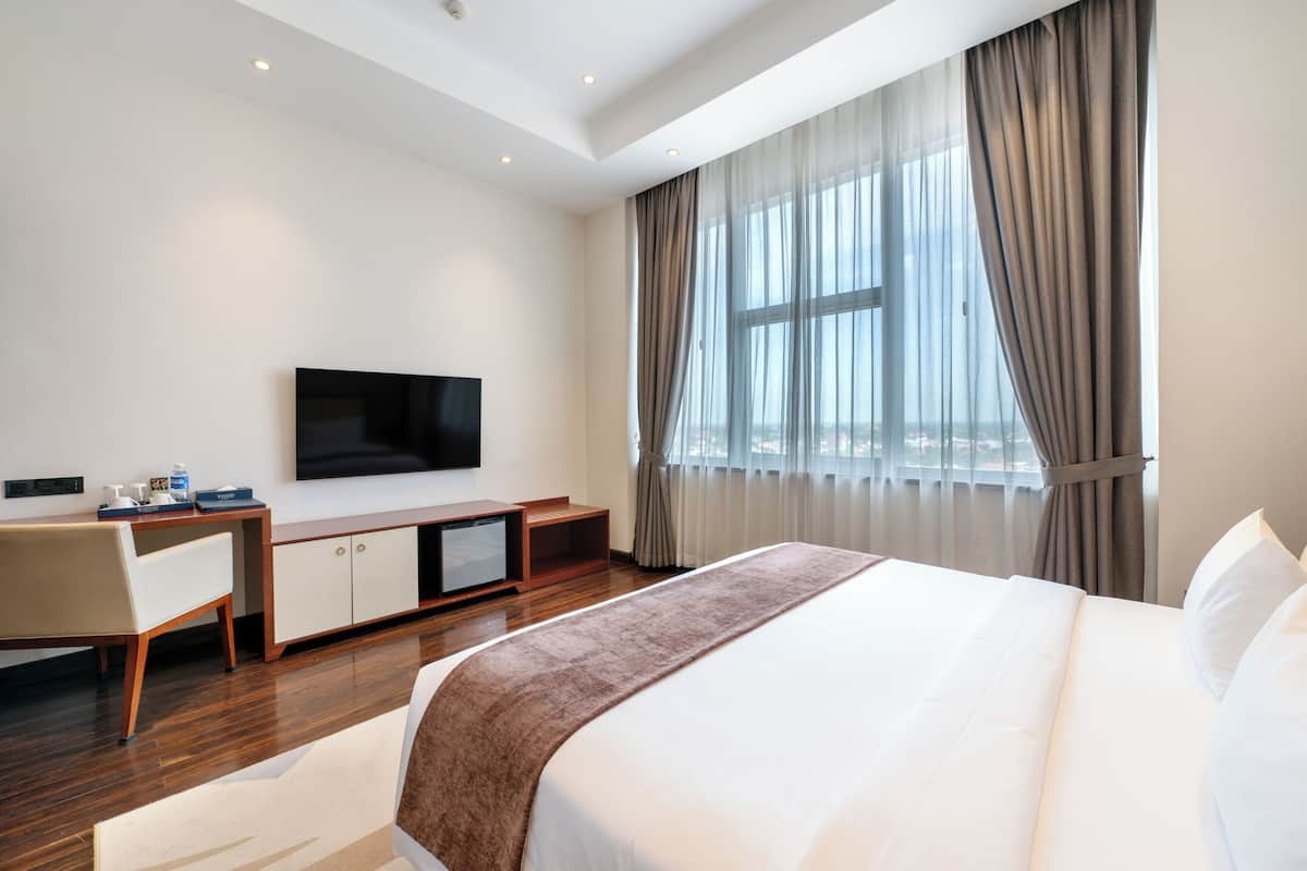 Hotelkamer met een groot bed, een flatscreen-tv, een bureau met stoel en een raam met gordijnen.