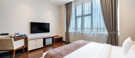 Una habitación de hotel con una cama grande, un televisor de pantalla plana, un escritorio con una silla y una ventana con cortinas.