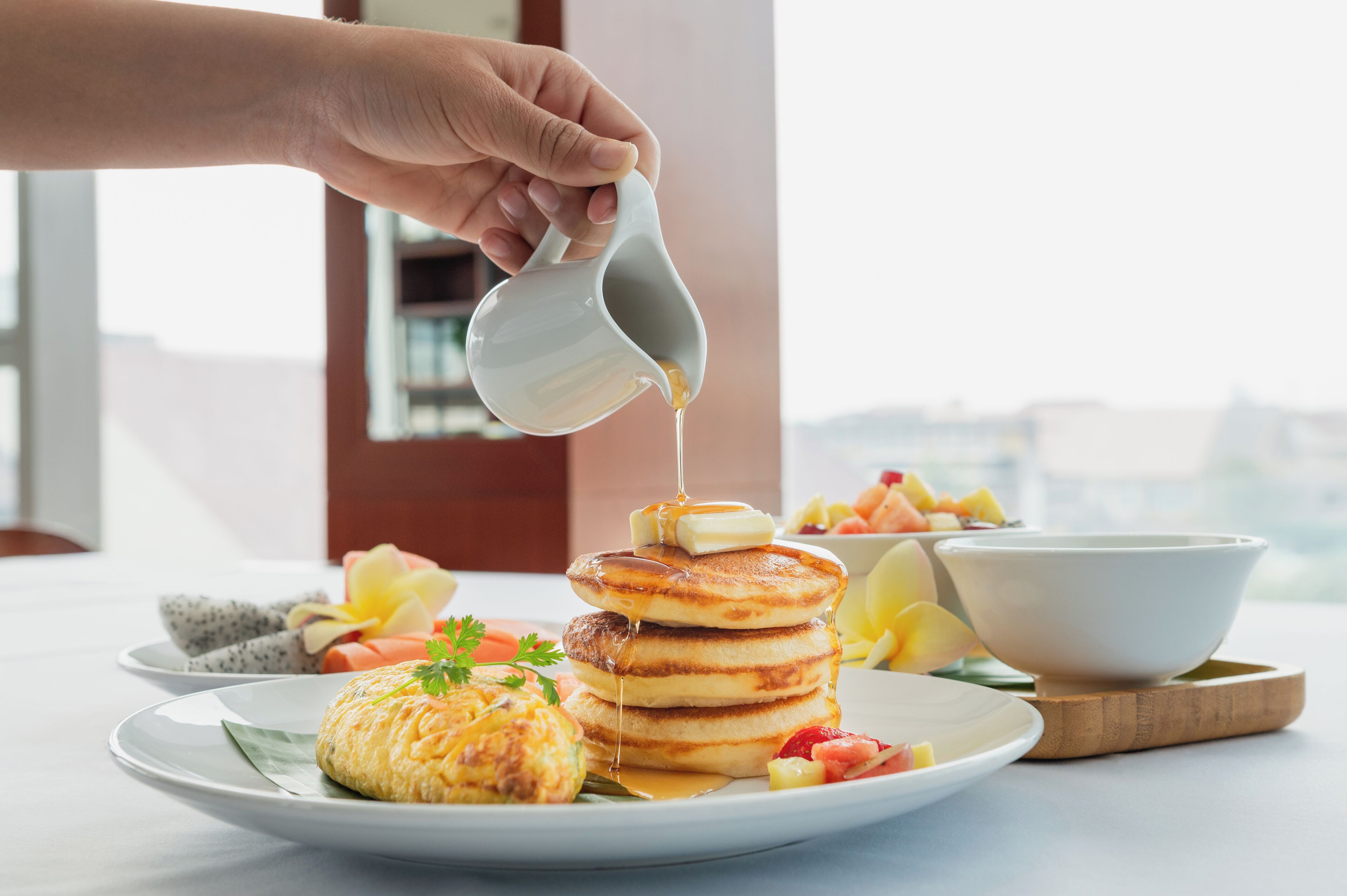 A breakfast plate with pancakes, a muffin, and a bowl of fruit.