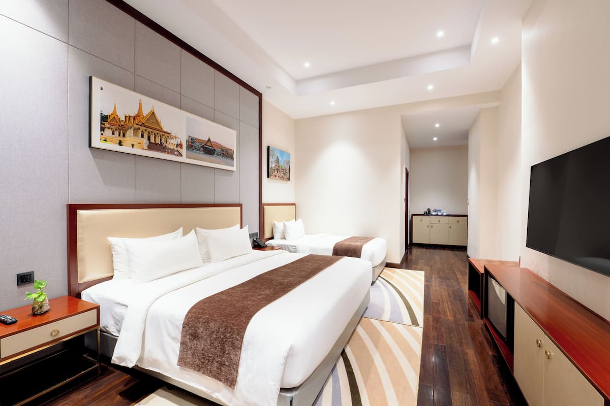 Een hotelkamer met een groot bed, een televisie, een klein bureau en een afbeelding van een tempel aan de muur.