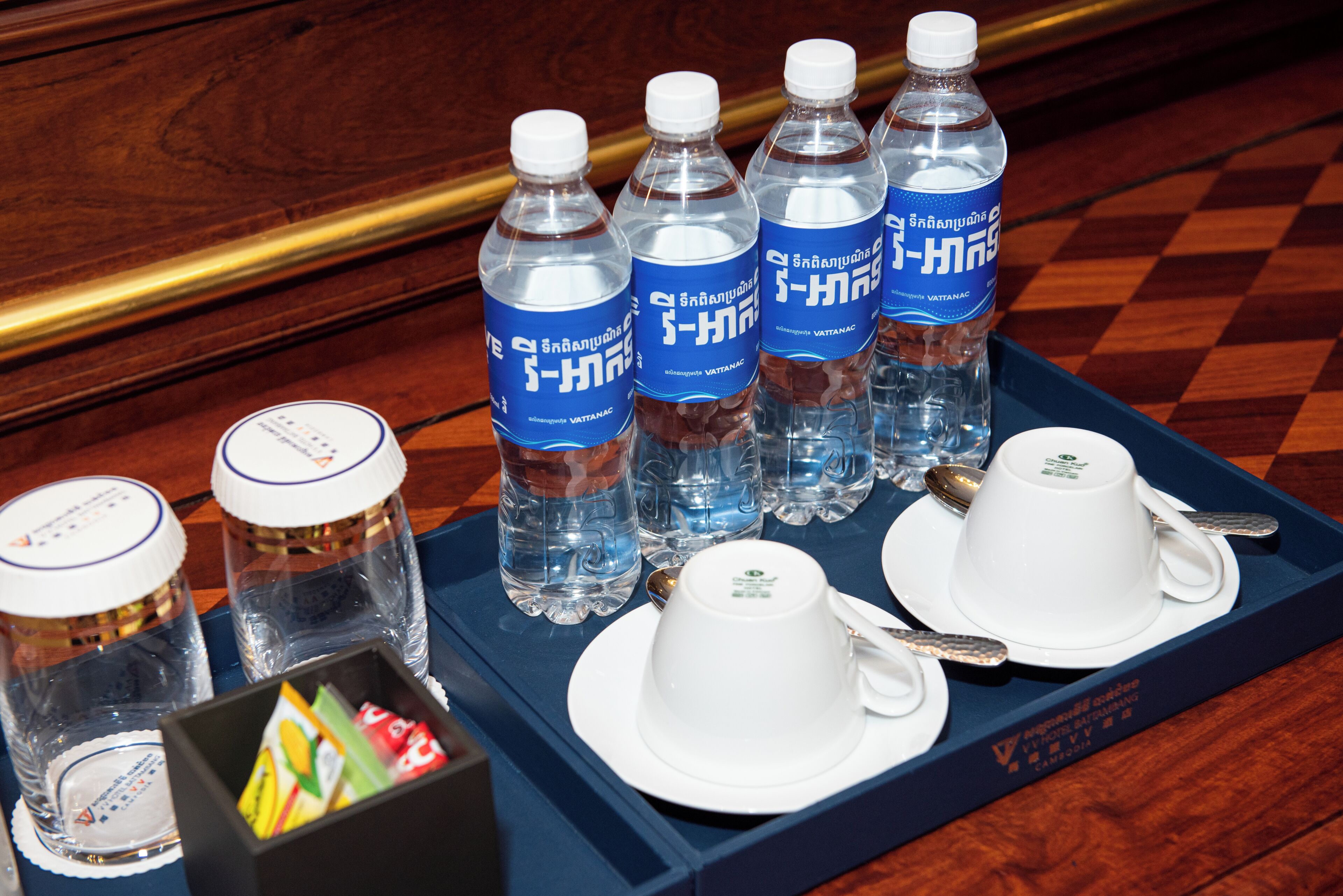 A tray with water bottles, white cups, and a box of snacks on a wooden table.