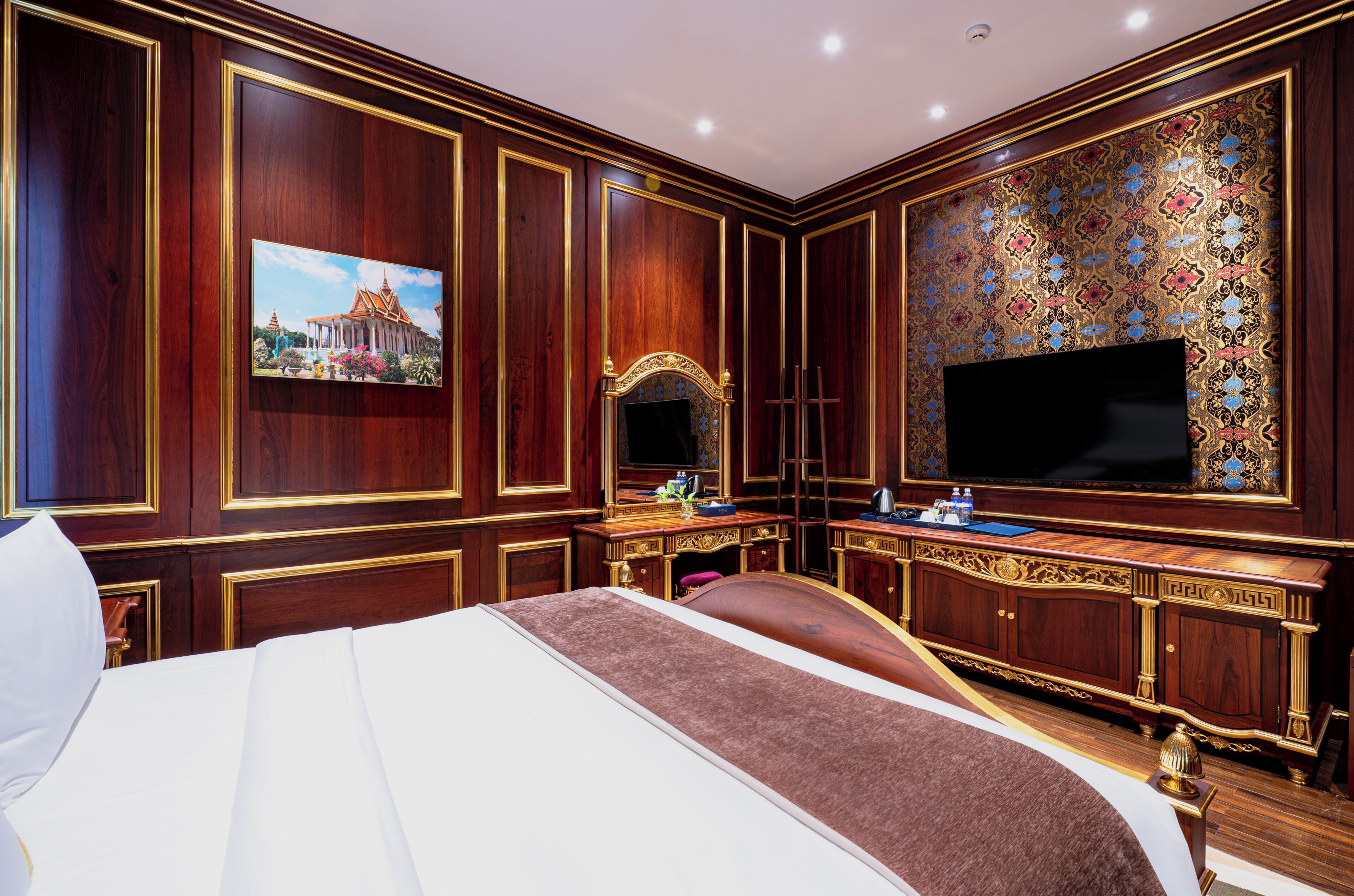 Una lujosa habitación de hotel con una cama grande, televisión, escritorio con silla y un detalle decorativo en la pared.