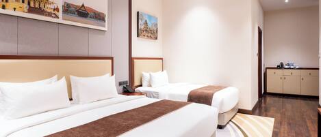 A hotel room with two beds, a desk, a wardrobe, and wall art depicting buildings.