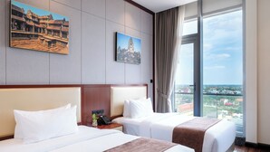 Une chambre d’hôtel avec deux lits, une grande fenêtre donnant sur la ville et deux tableaux encadrés accrochés au mur.