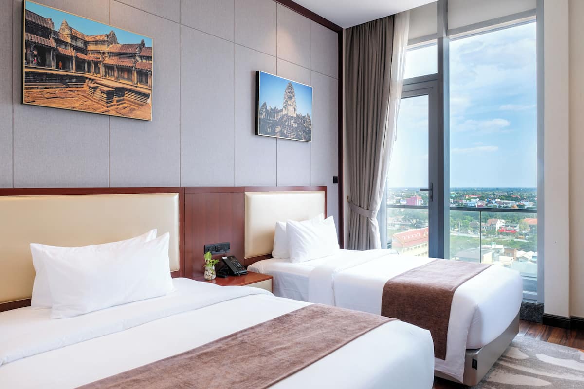 Een hotelkamer met twee bedden, een groot raam met uitzicht op de stad, en twee ingelijste foto’s aan de muur.