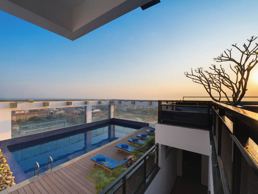 A rooftop pool with lounge chairs, a view of the city, and a balcony with a railing.