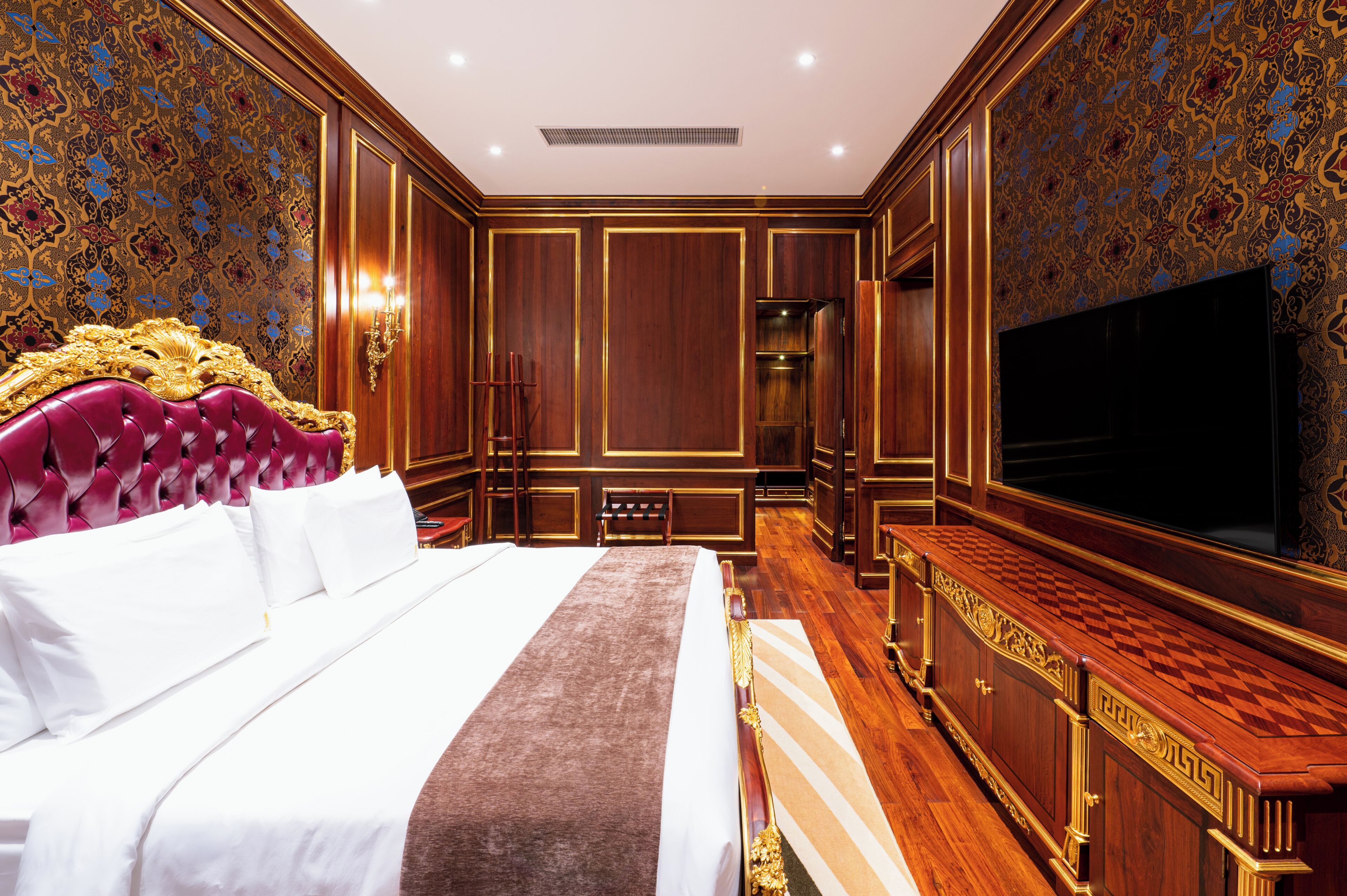 A luxurious hotel room with a large bed, a television, and ornate wood paneling.