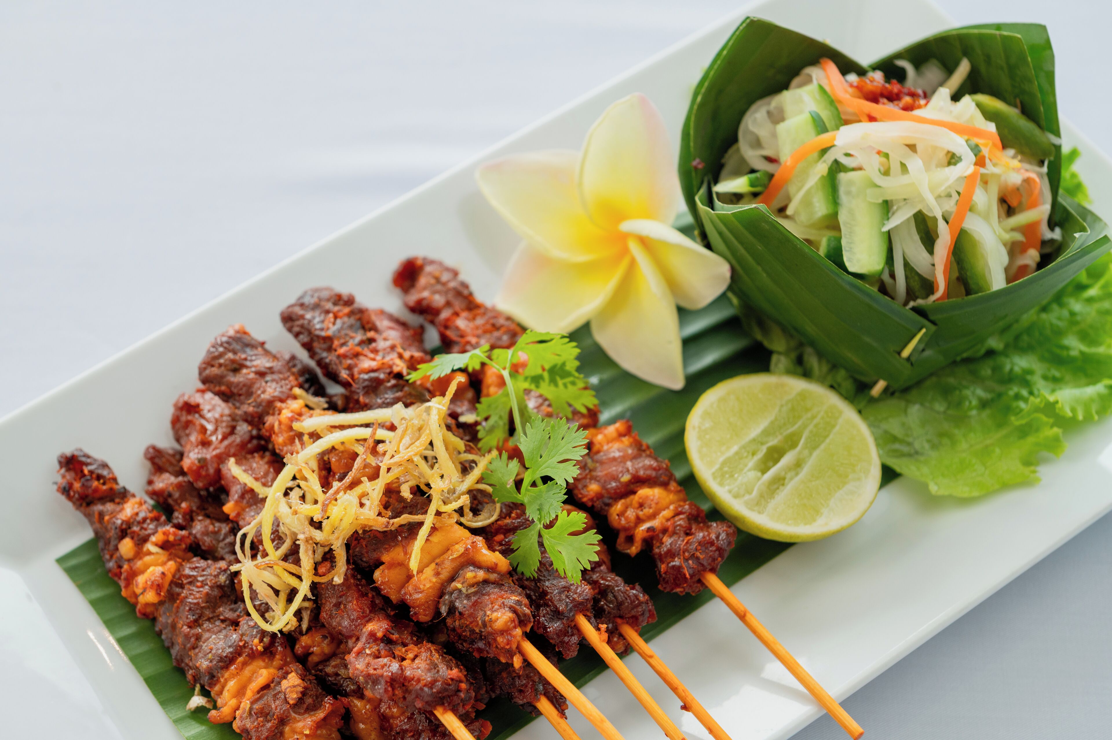 A plate of skewered meat garnished with herbs and a side salad in a leaf bowl.