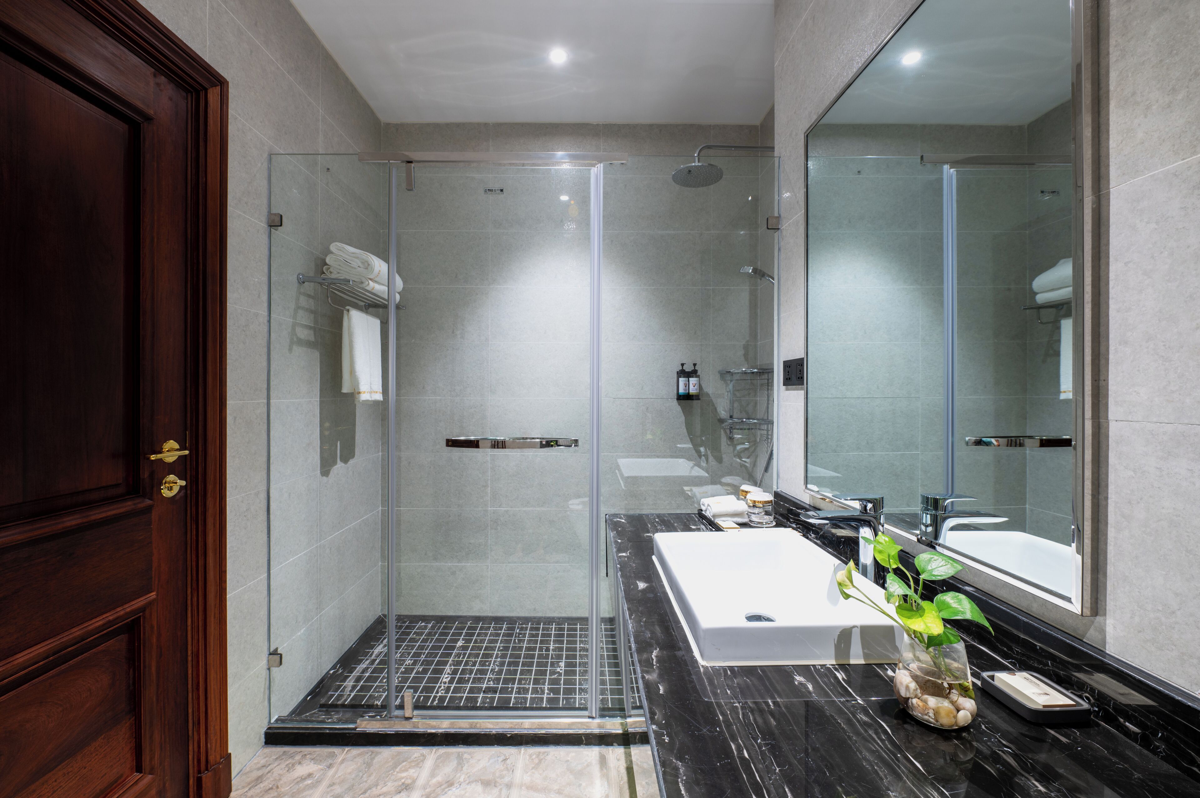 A modern bathroom with a glass-enclosed shower, a large mirror, and a marble countertop.