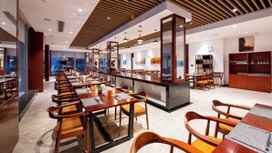 Un restaurant moderne avec des tables et des chaises en bois, un comptoir central et une vue sur le paysage urbain.