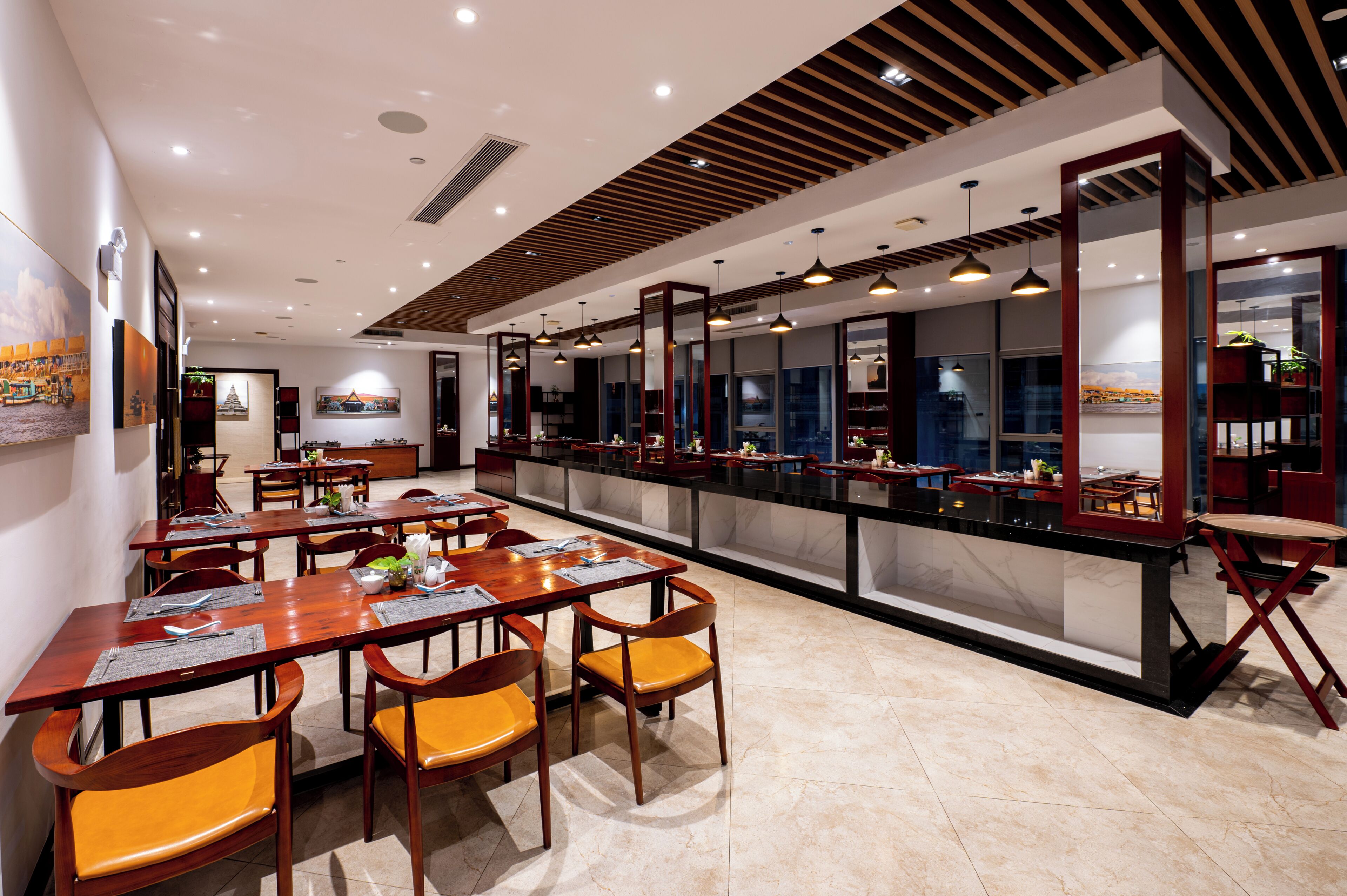 A modern dining area with wooden tables and chairs, a long counter, and pendant lighting.