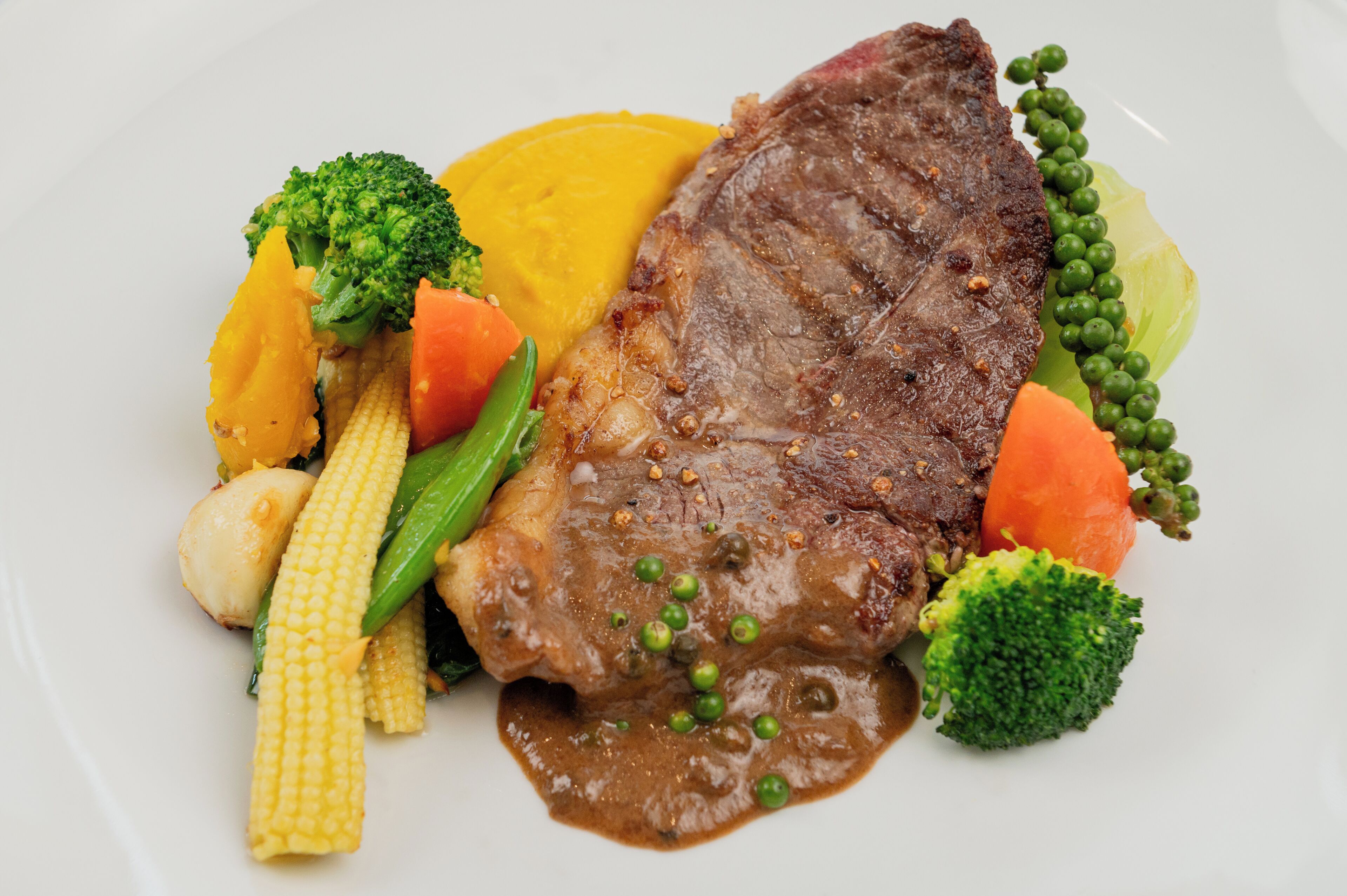 A plate with a steak, corn, broccoli, carrots, and peas.