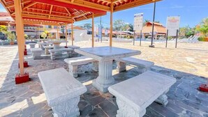 A covered outdoor seating area with stone tables and benches, surrounded by a stone-paved ground. - Villa Paraíso Mango 4 (Jacó)