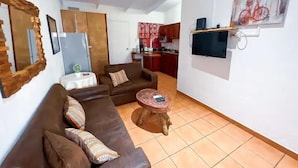 A living room with a brown sofa, a small round coffee table, and a TV mounted on the wall. - Villa Paraíso Mango 4 (Jacó)