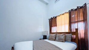 A bedroom with a bed, curtains, a nightstand, and a lamp. - Villa Paraíso Mango 4 (Jacó)