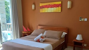 A spacious bedroom with a large bed, a wooden headboard, a bedside table with a lamp, and a view of the outdoors. - Cosy apartment unit in a triplex at less 100m from the beach with a common pool (Flic en flac)