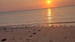 A beach with footprints leading to the water, a boat in the distance, and the sun setting over the horizon. - Cosy apartment unit in a triplex at less 100m from the beach with a common pool (Flic en flac)