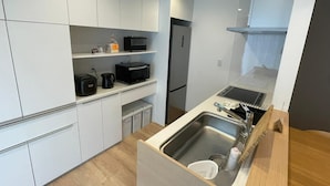 Una cocina compacta con gabinetes blancos, un lavamanos de acero inoxidable y un microondas en la encimera.