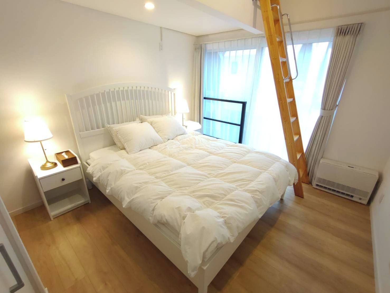Une chambre à coucher avec un lit, une table de chevet, une lampe, une fenêtre avec des rideaux et une échelle.
