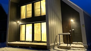 Una casa moderna de dos pisos con techo inclinado y ventanas amplias, rodeada de nieve.